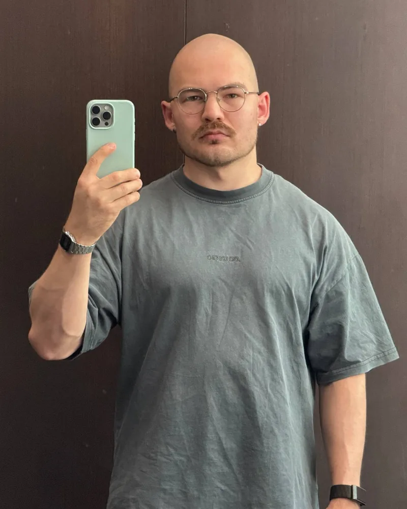 A man in a faded black oversized tee with OBRIGADO. embroidered tone on tone