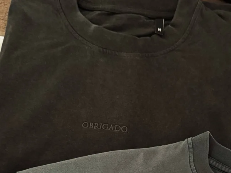 Close-up of a new Vintage Black tee: collar, size tag and OBRIGADO. tone on tone